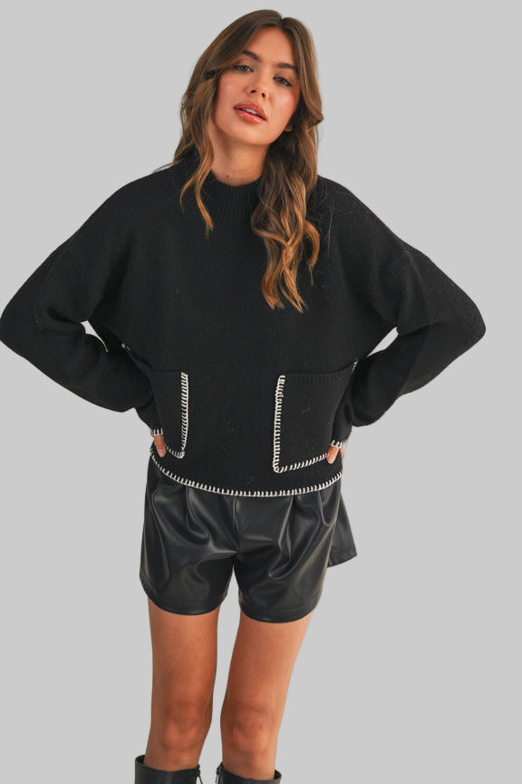 Woman wearing a black sweater with white trim and black shorts on a beige background