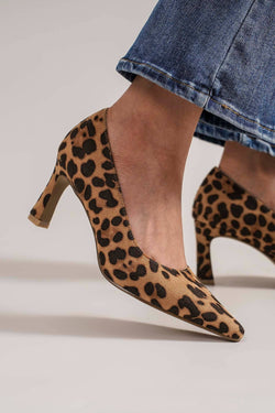 Leopard print high heels worn with a denim skirt on a neutral background
