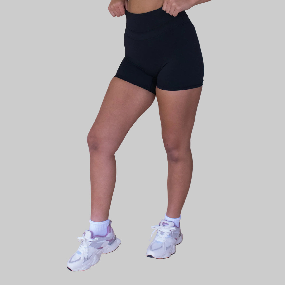 Person wearing black high-waisted shorts and white sneakers on a beige background