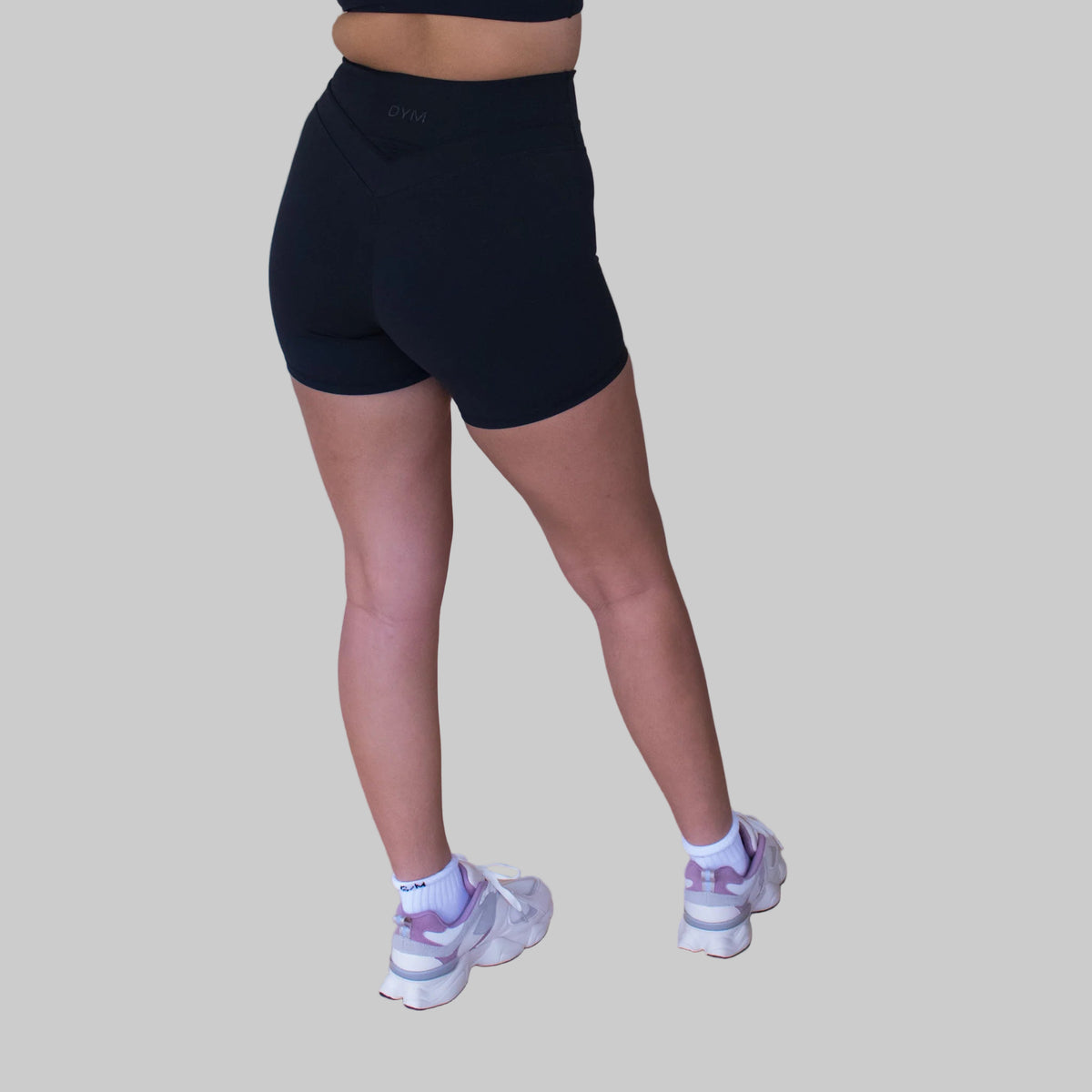 Person wearing black athletic shorts and white sneakers on a beige background