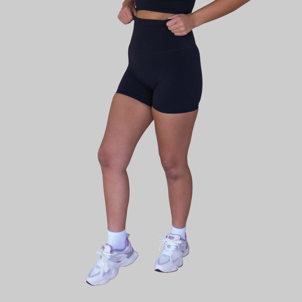 Person wearing black athletic shorts and white sneakers on a beige background