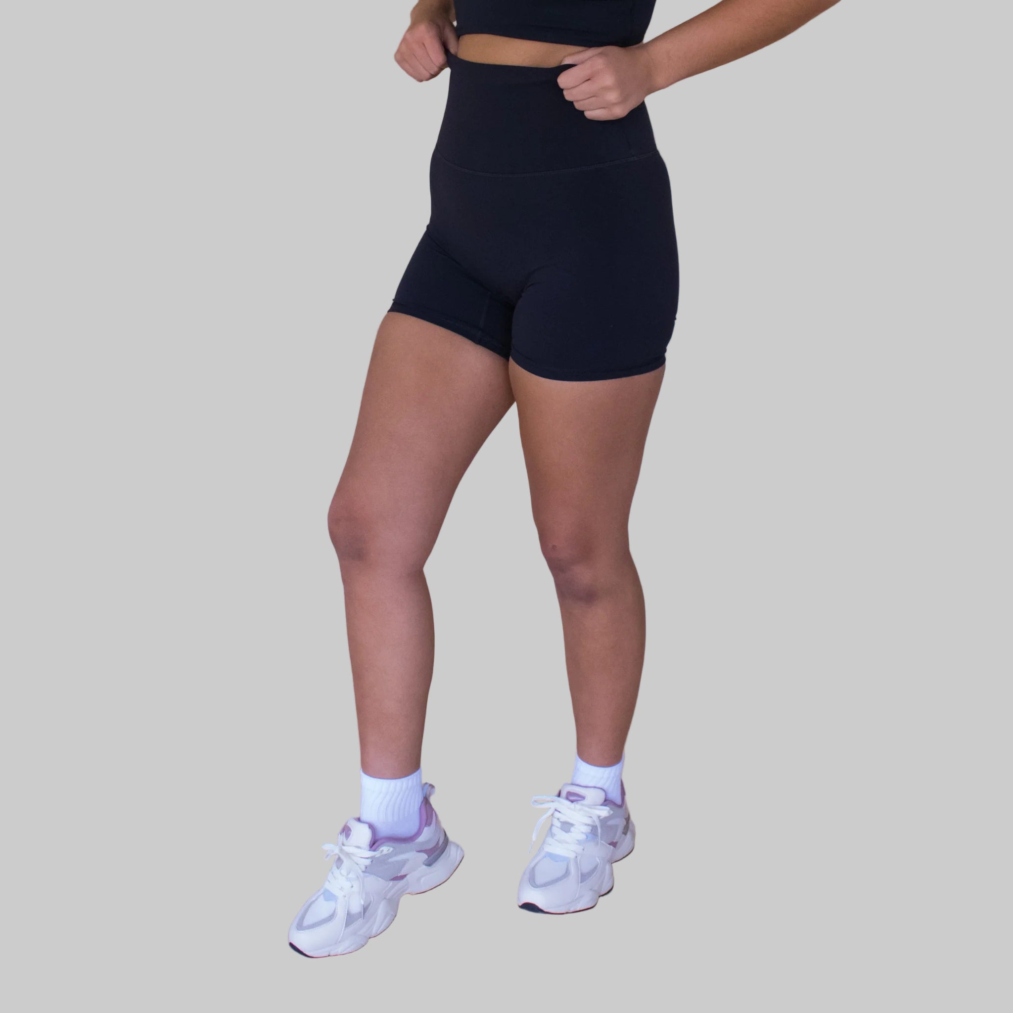 Person wearing black athletic shorts and white sneakers on a beige background