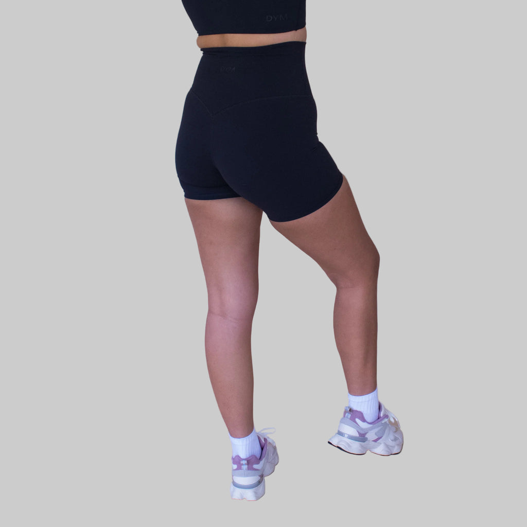 Person wearing black high-waisted shorts and white sneakers on a beige background