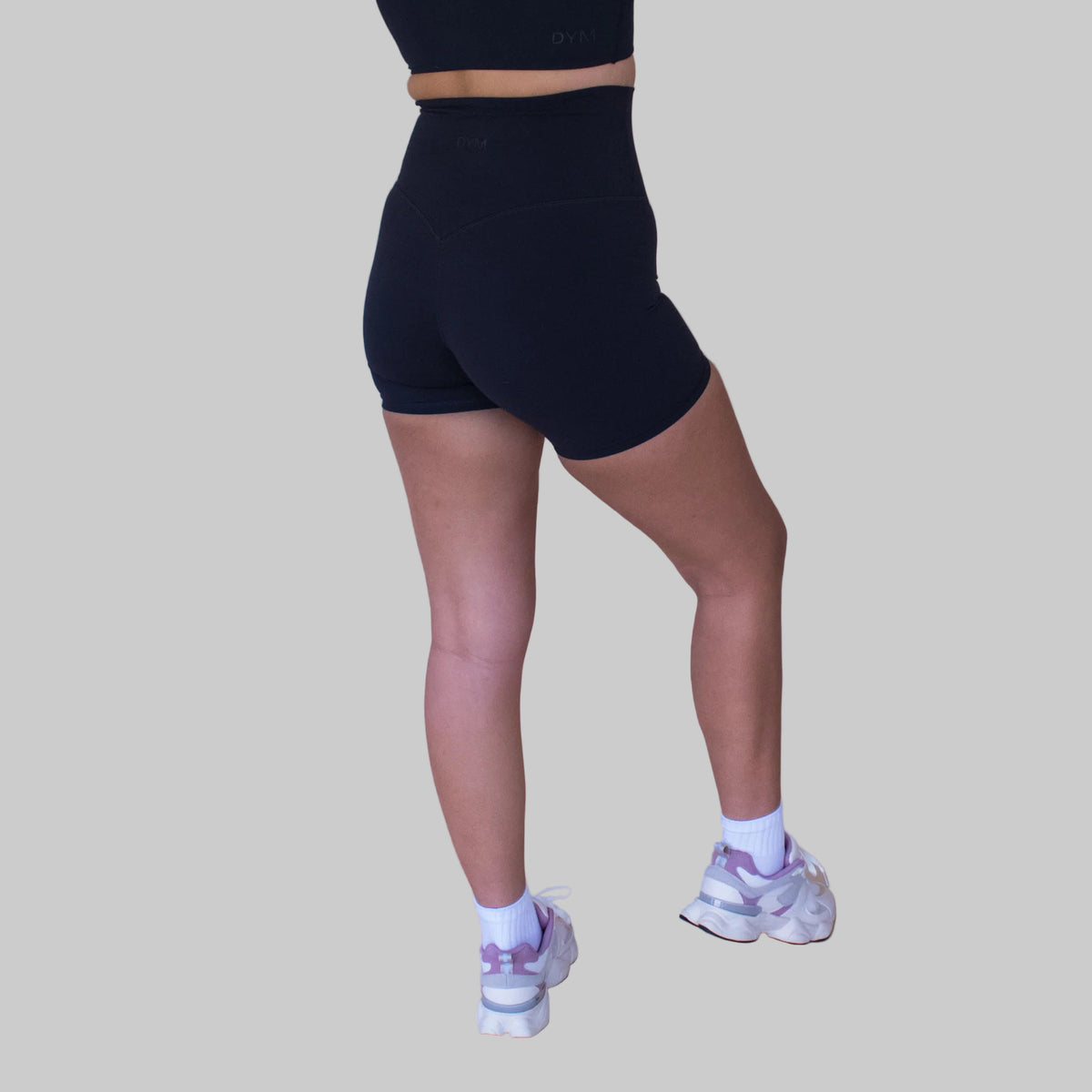 Person wearing black high-waisted shorts and white sneakers on a beige background