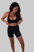 Woman wearing a black sports bra and shorts on a beige background