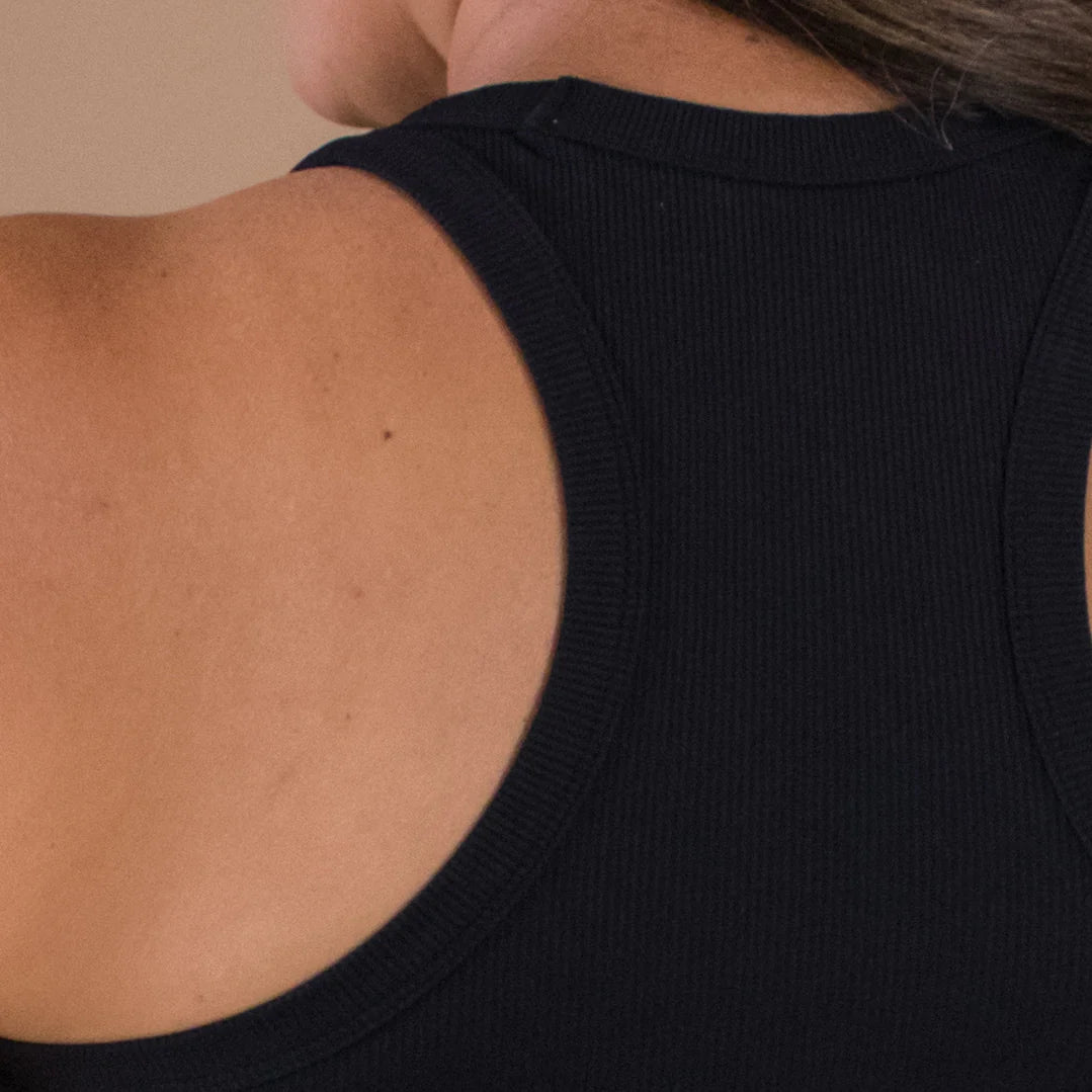 Close-up of a person wearing a black sleeveless top against a beige background