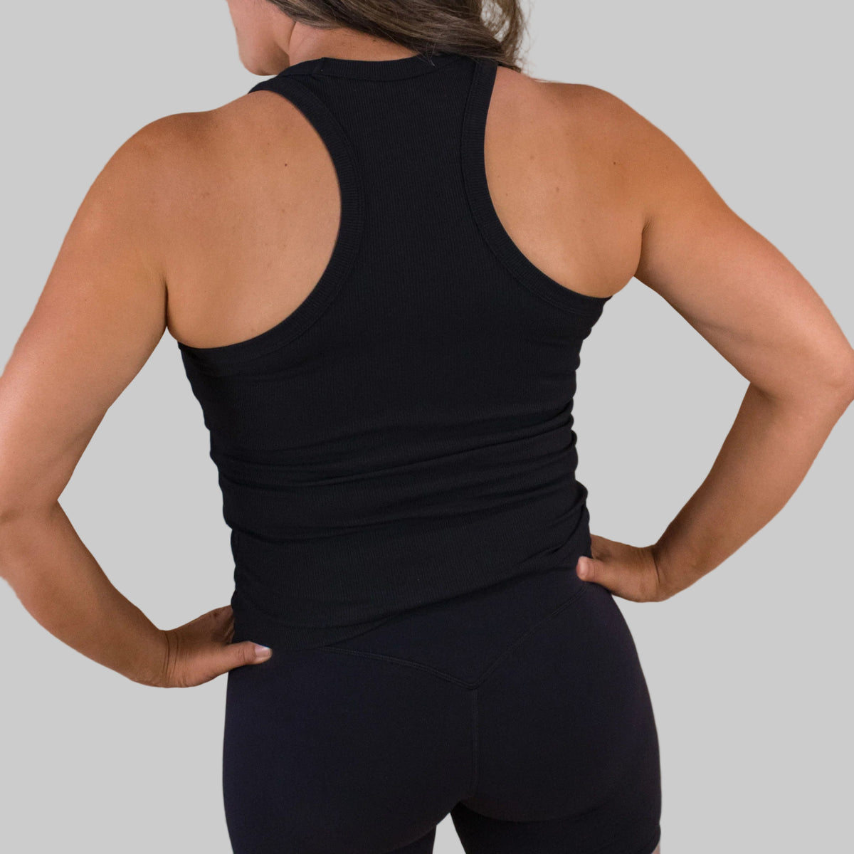 Person wearing a black tank top and leggings against a beige background