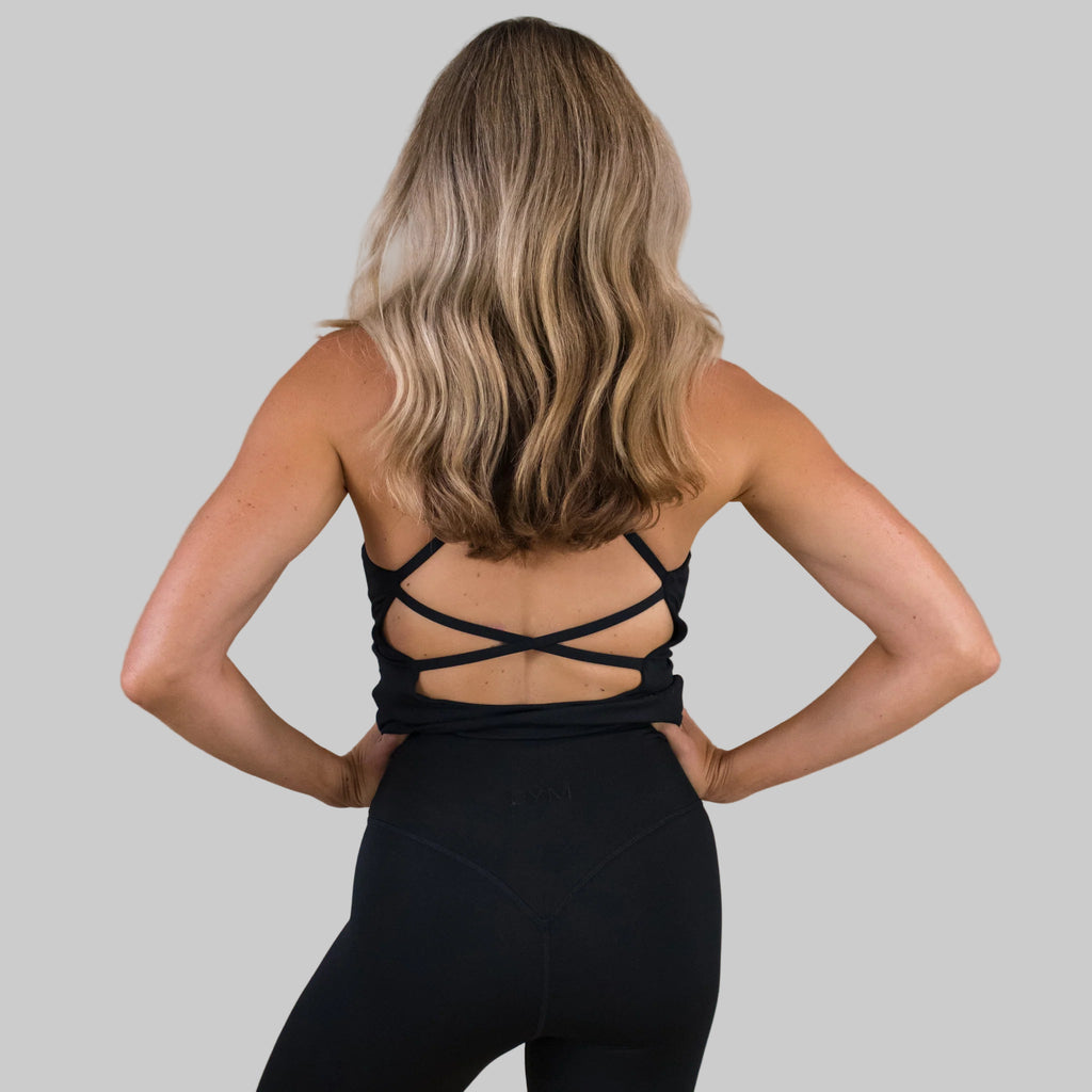 Person wearing a black strappy top and leggings against a beige background