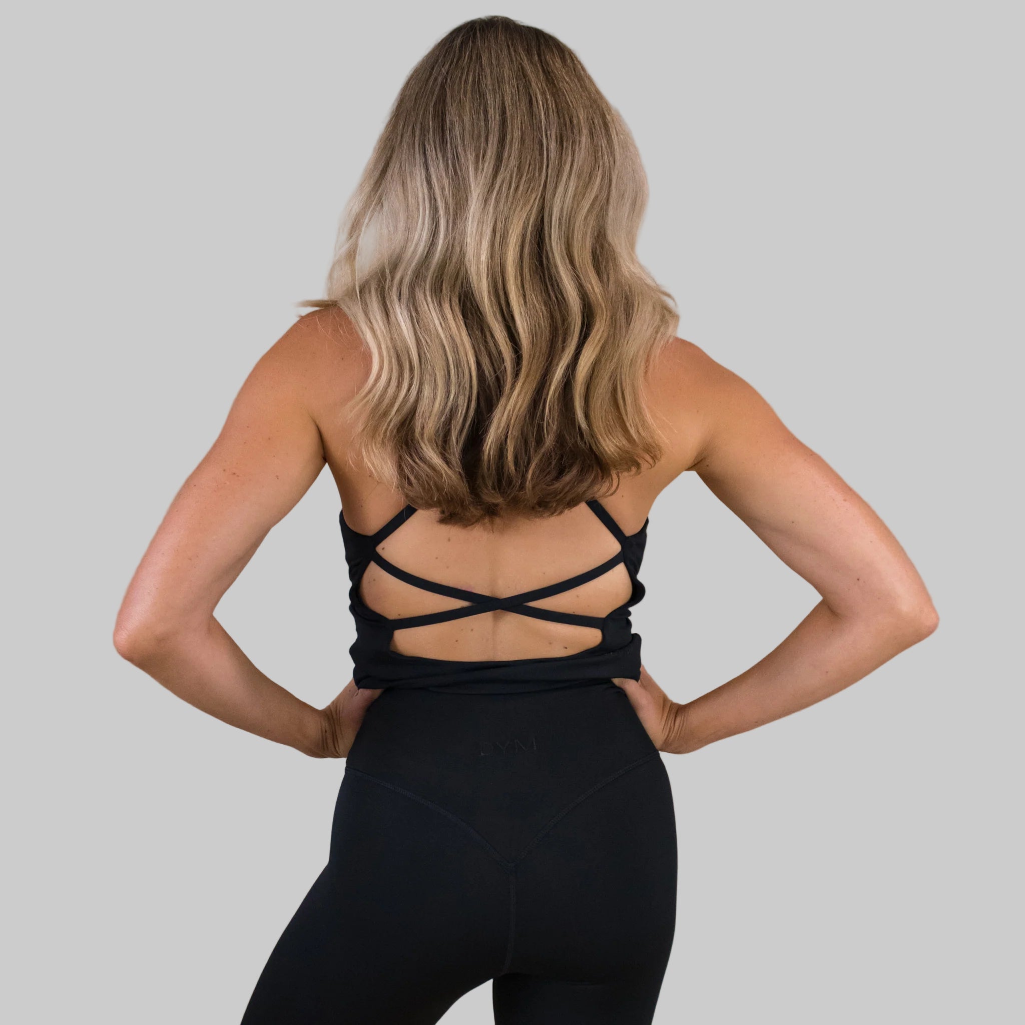 Person wearing a black strappy top and leggings against a beige background