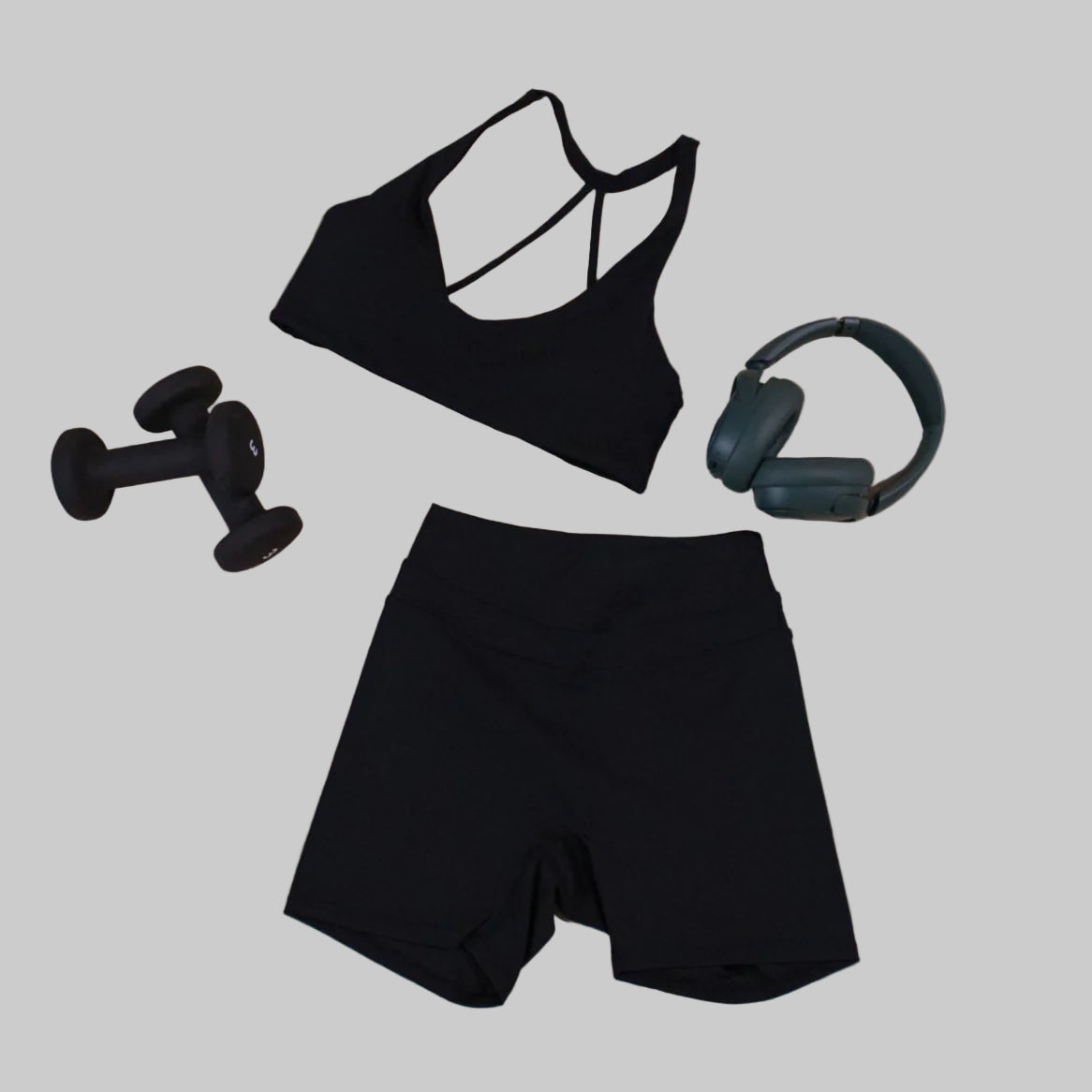 Black sports bra, shorts, dumbbells, and headphones on a beige background